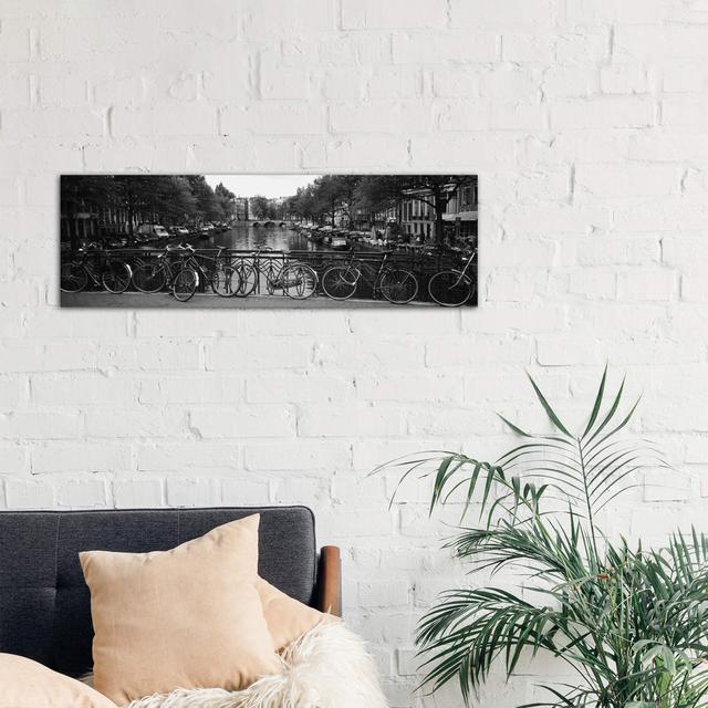 Bicycle Leaning Against A Metal Railing On A Bridge, Amsterdam, Netherlands - Wrapped Canvas Panoramic Print Brayden Studio Size: 40.64cm H x 121.92cm on Productcaster.